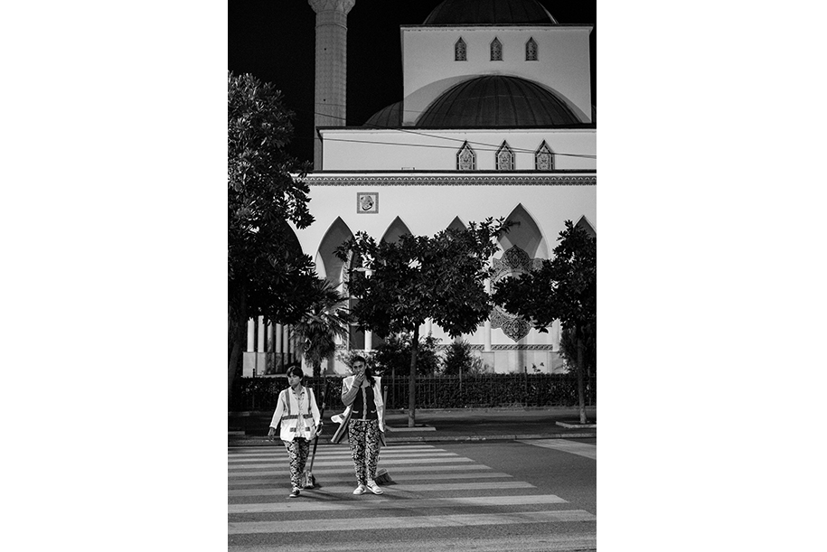 Black and white work photo of two cleaning ladies. Crossing a pedestrian crossing with a church on the background.