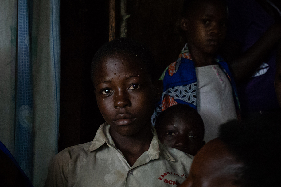 Travel portrait of a African boy in a dark living room. Rain drips are shown on his face. Ellis Photography.